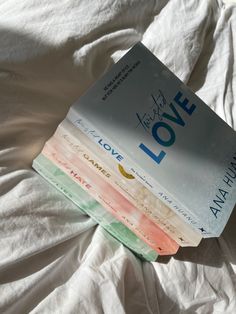 a stack of books sitting on top of a white sheet covered bed next to each other