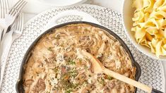 a skillet filled with pasta and mushrooms on top of a white plate next to silverware