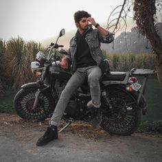 a man sitting on top of a motorcycle next to a tree