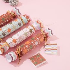 three rolls of wrapping paper tied together with twine on pink surface next to pine cones