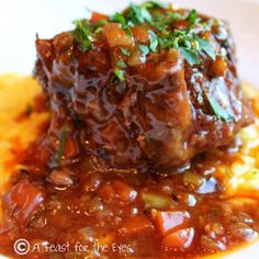 a white plate topped with meat covered in sauce and garnished with parsley