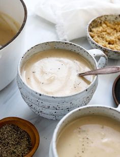 three bowls filled with soup next to two spoons on a white tablecloth covered surface