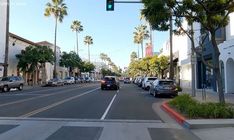 cars are driving down the street in front of buildings and palm trees on both sides