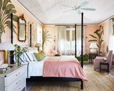 a bedroom decorated in pink and white with palm leaves on the walls, bedding, dressers, lamps, and mirror