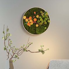 a clock with moss and flowers on the wall next to a vase filled with flowers