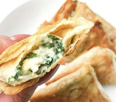 a hand is holding up some food on a white plate and it looks like they have spinach in them