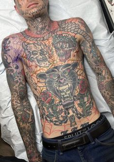 a tattooed man laying in bed with tattoos on his body and chest, looking at the camera