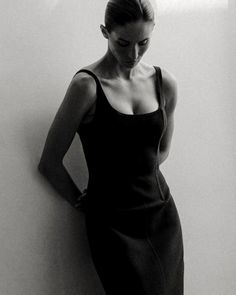 a black and white photo of a woman leaning against a wall with her hands on her hips