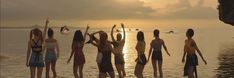 six girls standing in the water at sunset with their arms up and hands raised above their heads