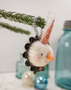 a christmas ornament hanging from a tree branch with ornaments around it and a jar in the background