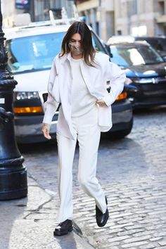 a woman in white is walking down the street with her hand on her hip and wearing black shoes