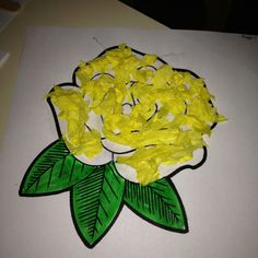 a paper plate with yellow flowers on it and green leaves in the middle, sitting on a white surface