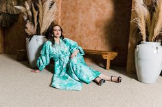 a woman sitting on the floor in front of two large vases with plants behind her