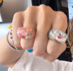 a woman with two rings on her fingers pointing at the camera while wearing a white t - shirt