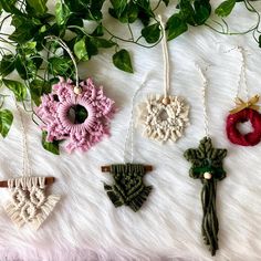 four crocheted ornaments are hanging on a white furnishing with greenery