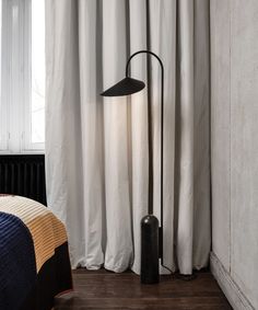 a bed room with a neatly made bed and a tall lamp next to the window