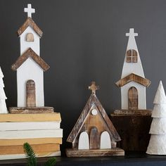 three small wooden churches sitting on top of a shelf next to books and pine trees