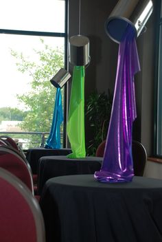 colorful vases sitting on top of a table in front of a large window with red chairs