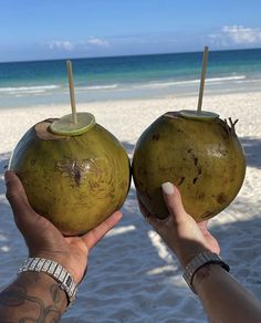 two people holding up coconuts on the beach