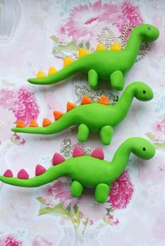 two green toy dinosaurs sitting next to each other on a pink flowered tablecloth