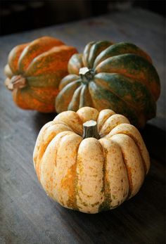 three pumpkins sitting on top of a wooden table