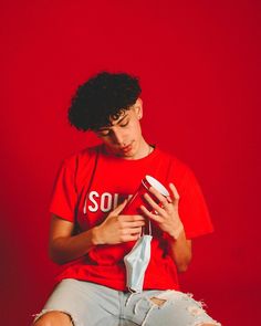 a person sitting on a chair with a cell phone in their hand and a red wall behind them