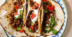 three tacos on a plate with sour cream and tomatoes