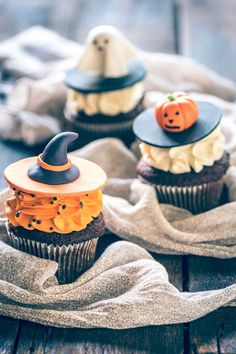 three cupcakes decorated like witches and pumpkins on top of a cloth covered table