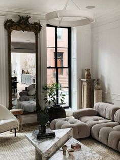 a living room filled with furniture and a large mirror on top of the wall next to a window