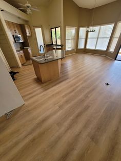 an empty living room with hard wood flooring and large open kitchen area in the background