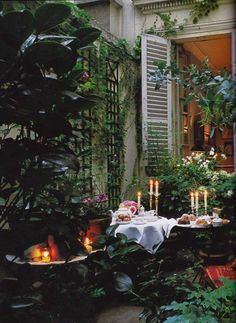 an outdoor dining area with candles on the table and potted plants in the background