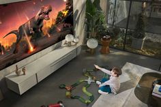 a little boy playing with toys in front of a television screen that has dinosaurs on it