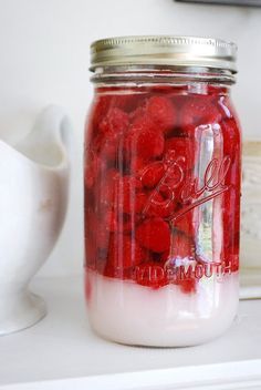 a mason jar filled with raspberries sitting on top of a white shelf