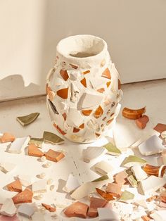 a white vase sitting on top of a table covered in broken pieces of glass and paper