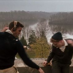 two men with headphones on standing next to each other in front of a lake