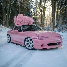 a pink car parked in the snow with a bunch of flowers on top of it