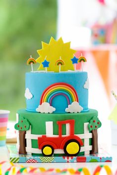 a birthday cake decorated with rainbows, stars and a train on the top is sitting on a table