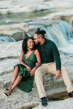 a man and woman are sitting on rocks near a waterfall