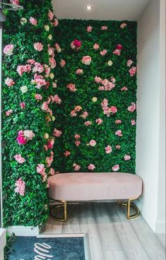 a pink bench sitting in front of a green wall with flowers growing on it's sides