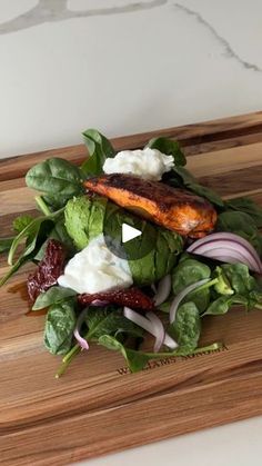 a wooden cutting board topped with a salad and fish on top of it's side