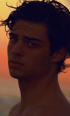 a man with no shirt on standing in front of an orange and blue sky at sunset