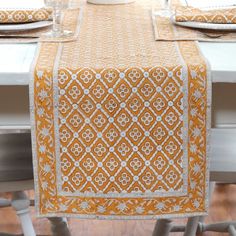 an orange and white table runner on top of a dining room table with place settings