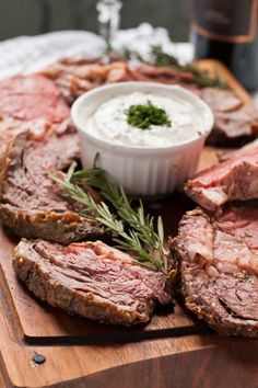 a wooden cutting board topped with sliced meat and dip