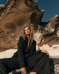 a woman sitting on top of a rock next to a large rock formation in the desert