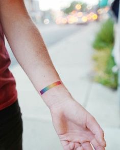 a person with a rainbow wristband on their arm pointing to the side while standing on a sidewalk