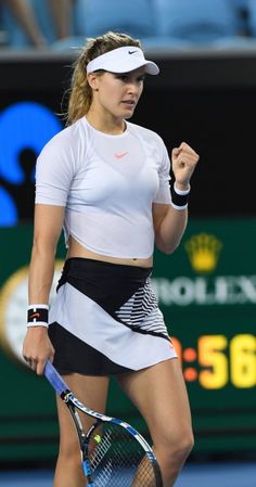 a woman holding a tennis racquet on top of a tennis court with people in the background