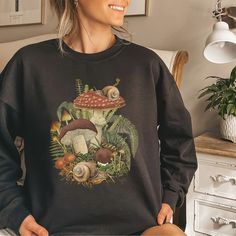 a woman wearing a black sweatshirt with mushrooms and ferns on it, smiling at the camera