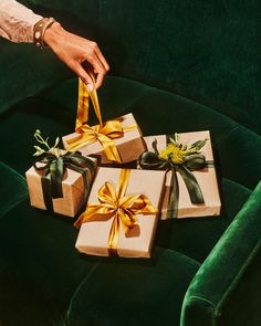 three wrapped presents are sitting on a green velvet couch with gold ribbons and bows tied around them