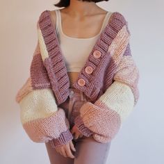 a woman wearing a pink and white sweater with buttons on the sleeves is standing in front of a wall