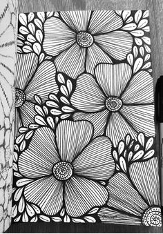 a black and white drawing of flowers on a piece of paper next to a pen